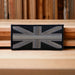 Black and grey metallic thread Union Jack GB embroidered sew-on flag patch with a hook and loop fastener backing on a wooden table