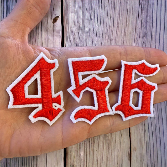 Red and white old english iron on patch numbers showing 4, 5 and 6 in a hand